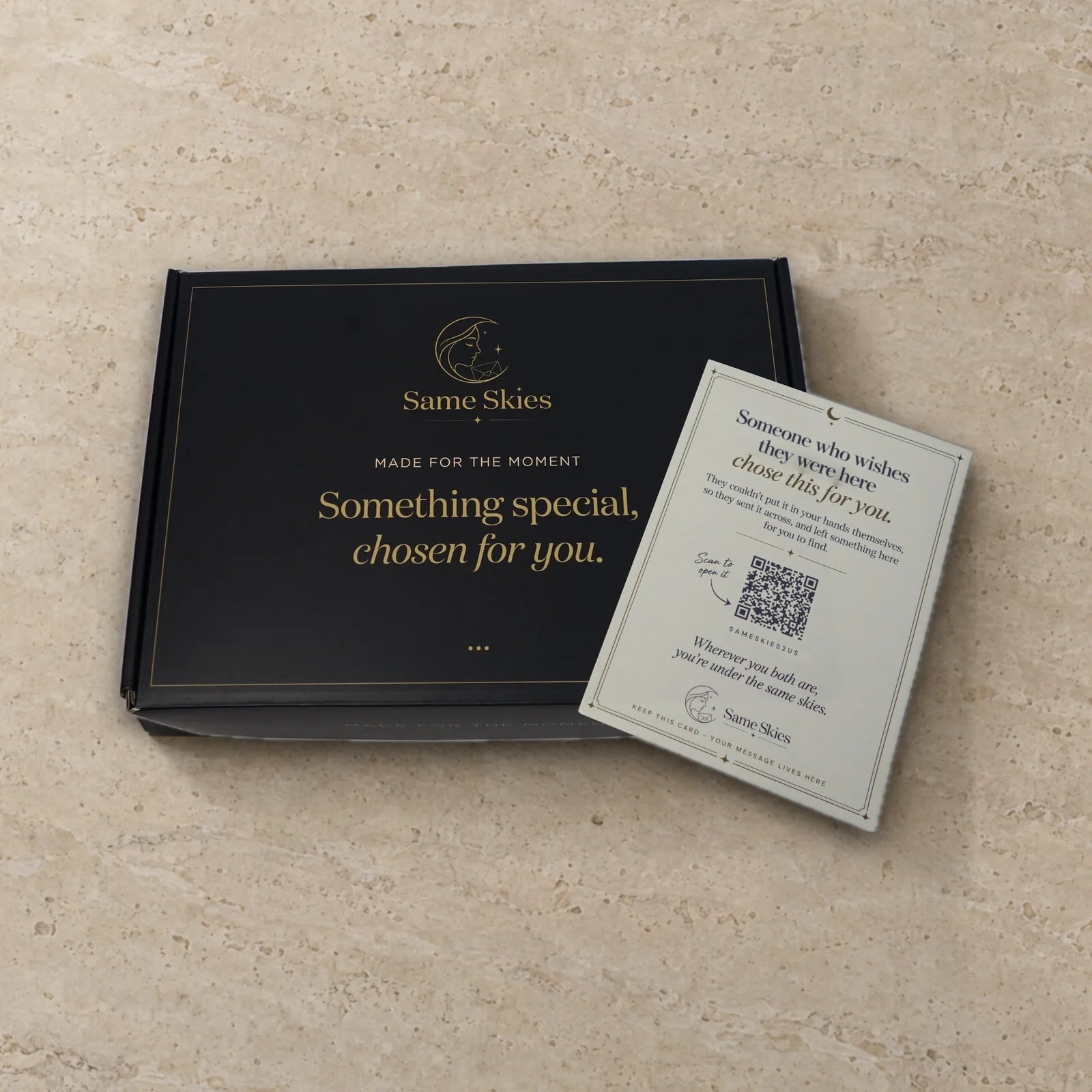 A closed Same Skies gift box printed with Something special, chosen for you, with the personal letter resting on it, on travertine stone